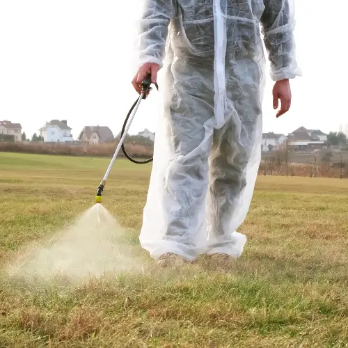 Technician wearing protective gear applying pest control treatment to grass in a residential area